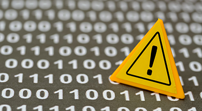 Yellow warning triangle with an exclamation mark placed on a blurred background of binary numbers, symbolizing a data breach, data exposure, or cybersecurity risk.