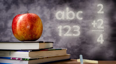 An apple on top of school books with a chalkboard in the background