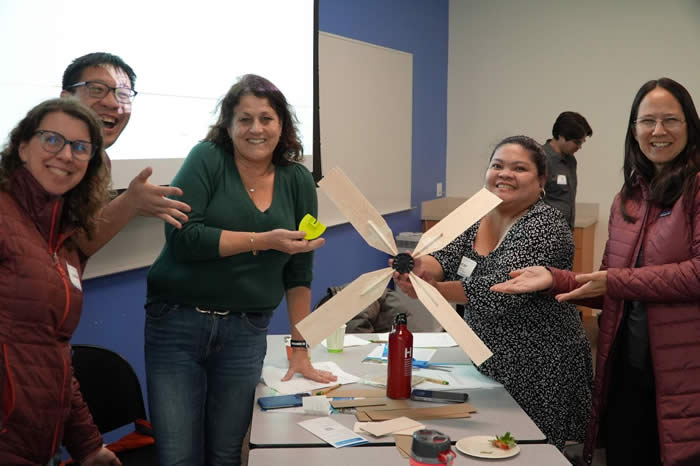 five people holding up a four-bladed fan