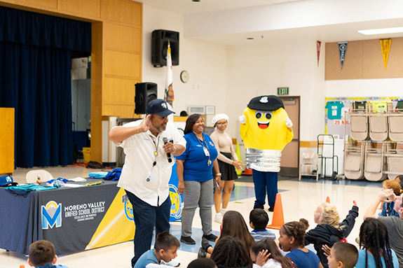 Picture of Moreno Valley Unified School District students listening to presenters and a light bulb mascot in a school hall