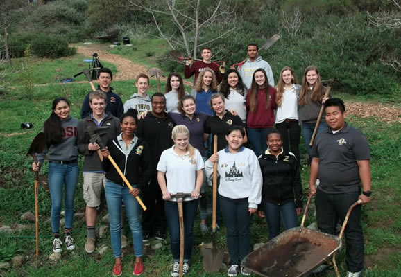 A group of students with gardening tools out in a field.