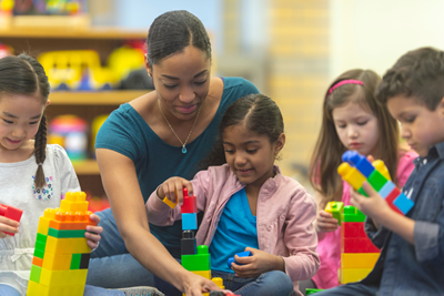 A teacher works with three young children who are using building blocks.